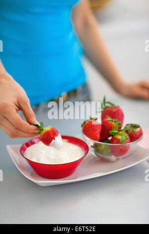 Primo piano sulla felice giovane donna di mangiare fragole con yogurt in cucina Foto Stock