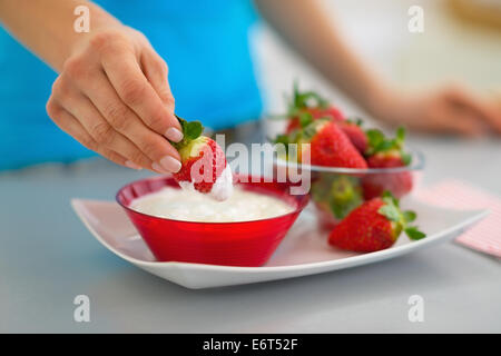 Primo piano sulla felice giovane donna di mangiare fragole con yogurt in cucina Foto Stock