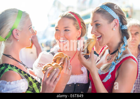 Amici in visita insieme fiera bavarese in costume nazionale griglie mangiare salsiccia in rotolo di pane Foto Stock