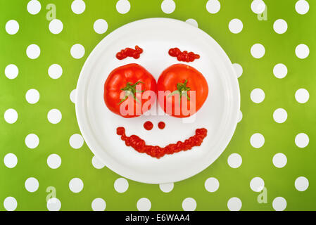 Ripe rosso dei pomodori e ketchup rendendo emoticon Smiley face servita su una piastra bianca sul tavolo per la cena. Foto Stock