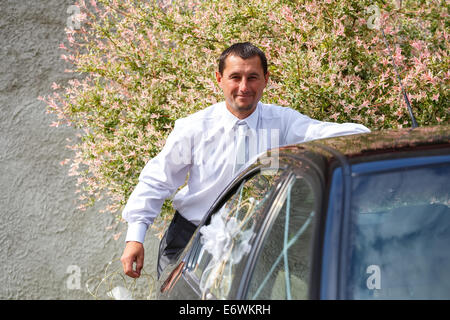 Sorridente groom la preparazione e la decorazione auto nel giorno di nozze Foto Stock