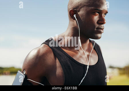 Close-up immagine di montare il giovane uomo che indossa gli auricolari focus per la sua esecuzione. African modello maschile che indossa gli auricolari per ascoltare la musica. Foto Stock