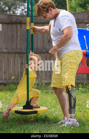 Nonna con una gamba protesico giocando su un set di swing con la sua nipote Foto Stock