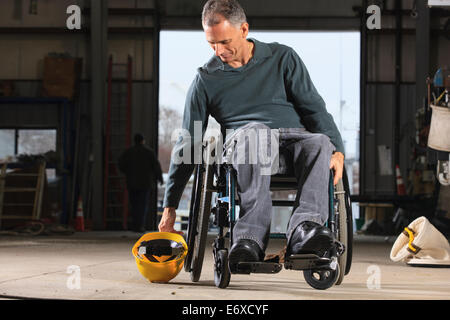 Ingegnere con lesioni del midollo spinale di prelevare il suo elmetto in officina Foto Stock