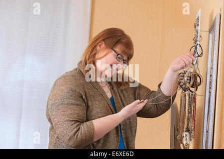 Donna che è legalmente cieco scegliendo gioielli a vestirsi in casa sua Foto Stock