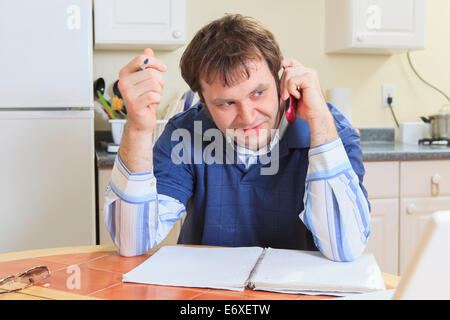 Programmatore con Aspergers lavorando sul suo computer da casa e parlando al telefono cellulare Foto Stock