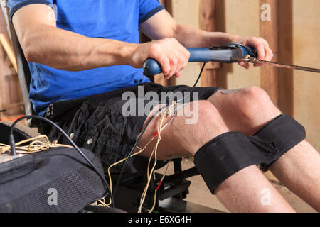 Uomo con lesioni del midollo spinale usando il Suo vogatore con uno stimolatore muscolare attaccata Foto Stock