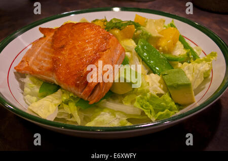 Deliziosa disseccata selvaggio del Pacifico di filetto di salmone su una fresca insalata di lattuga piselli della neve, arance e avocado in un condimento agli agrumi. Foto Stock