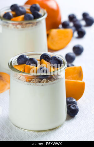 I vasetti di yogurt e rabboccato con mirtilli e pezzi di persimmon Foto Stock