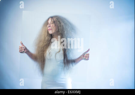 Una giovane donna con lunghi biondi capelli biondi che indossa un abito bianco tenendo un foglio di vetro diffusa nella parte anteriore del suo viso Foto Stock