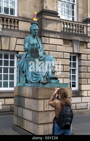 Una giovane donna fotografa la statua del David Hume con 'No parcheggio' cono sulla sua testa sul Royal Mile di Edimburgo, Scozia, Regno Unito Foto Stock