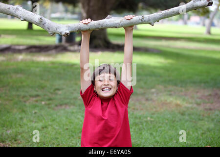 Felice ragazzo appeso a un ramo di albero presso il parco Foto Stock