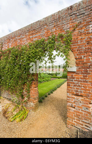 Arco della porta attraverso un vecchio muro di mattoni in il giardino murato a Felbrigg Hall, Norfolk con fiore della passione della vigna Foto Stock