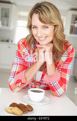 Metà donna età con caffè e biscotti a casa Foto Stock