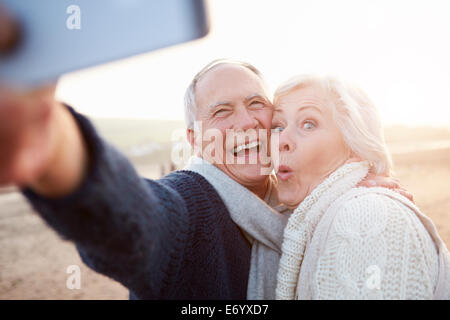 Coppia senior permanente sulla spiaggia prendendo Selfie Foto Stock