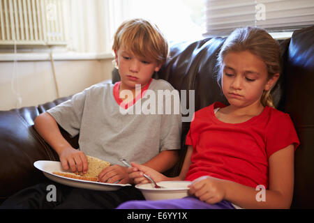 I bambini con dieta povera di mangiare pasto sul divano di casa Foto Stock