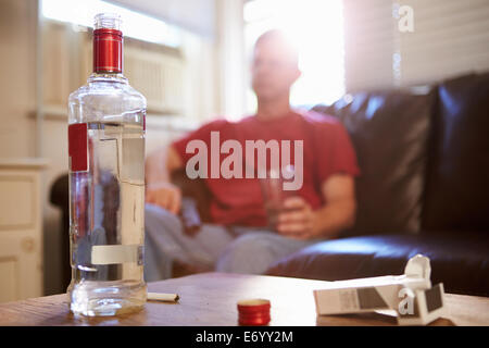 Uomo seduto sul divano con una bottiglia di vodka e sigarette Foto Stock
