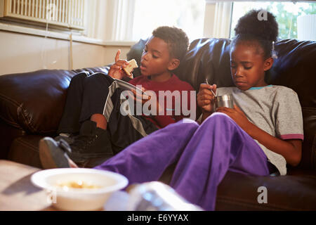 I bambini con dieta povera di mangiare pasto sul divano di casa Foto Stock