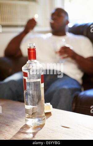 Uomo seduto sul divano con una bottiglia di vodka e sigarette Foto Stock