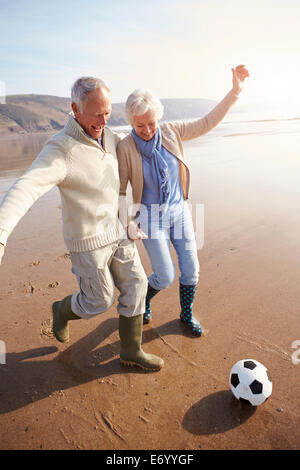 Coppia senior giocando a calcio sulla spiaggia invernale Foto Stock