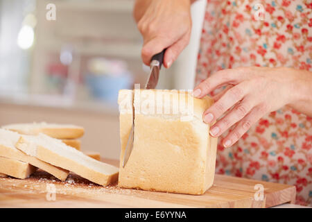 Close up della donna per affettare pagnotta di pane in cucina Foto Stock