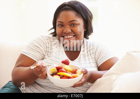 Donna sovrappeso seduti sul divano a mangiare frutta fresca Foto Stock