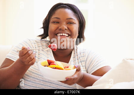 Donna sovrappeso seduti sul divano a mangiare frutta fresca Foto Stock