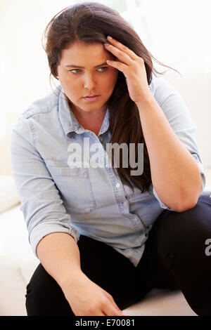 Premuto il sovrappeso donna seduta sul divano Foto Stock