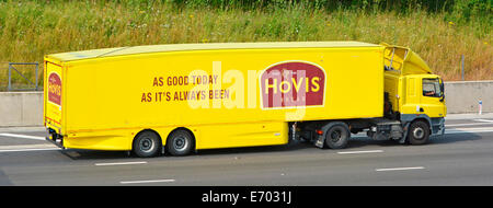 Vista laterale della distribuzione del pane giallo hgv catena di fornitura alimentare camion e conducente con pubblicità Hovis su rimorchio aerodinamico che guida su autostrada UK Foto Stock