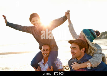 Gli uomini dando piggyback ride per donne sulla spiaggia Foto Stock