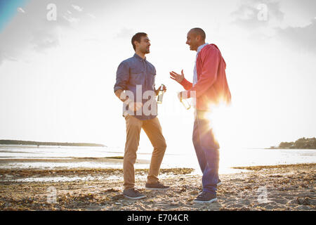 Gli uomini di bere birra e conversare sulla spiaggia Foto Stock