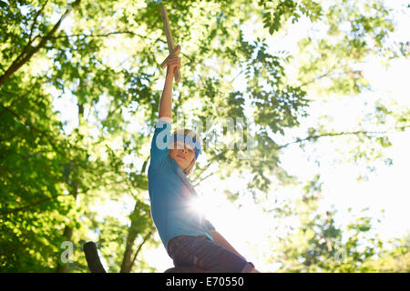 Un giovane ragazzo con spada giocattolo, seduto sul ramo di albero Foto Stock