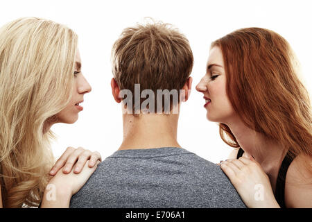 Ritratto in studio di due giovani donna whispering in giovane uomo le orecchie Foto Stock