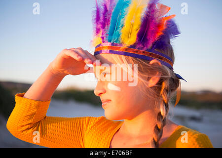 Close up della ragazza vestita come native american in piuma copricapo con mano gli occhi di ombreggiatura Foto Stock
