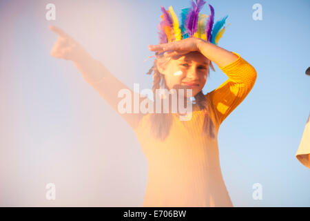 Ragazza vestita come native american in piuma copricapo con mano gli occhi di ombreggiatura e puntamento Foto Stock