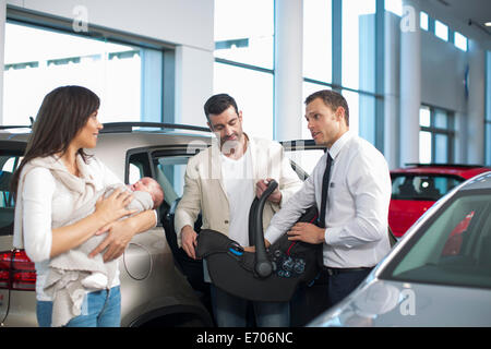 Venditore in chat a metà adulto giovane con baby girl in concessionaria auto Foto Stock