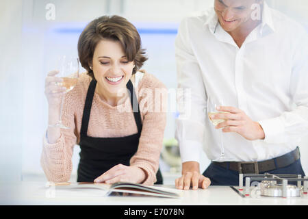 Paio di bere un bicchiere di vino bianco mentre la lettura del libro di ricette di cucina Foto Stock