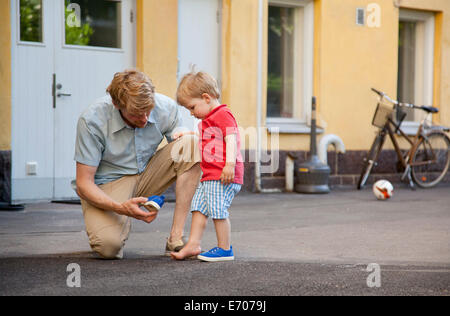 Padre dando toddler figlio una mano a mettere su il trainer in giardino Foto Stock