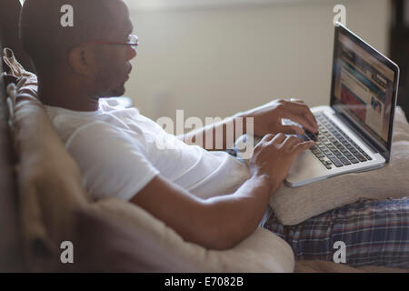 Metà uomo adulto, giacente sul letto, utilizzando laptop Foto Stock