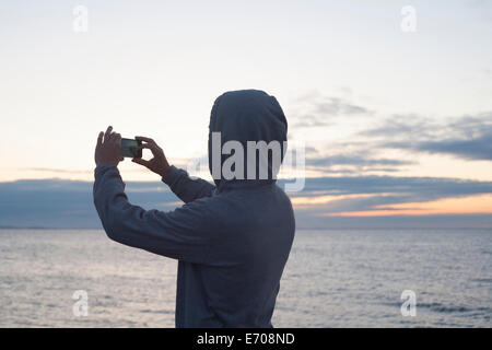 Metà uomo adulto in top con cappuccio a fotografare il mare con lo smartphone, Gloucester, Massachusetts, STATI UNITI D'AMERICA Foto Stock