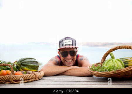 Ritratto di metà uomo adulto in berretto da baseball e sfumature sporgersi in avanti sul banco per picnic Foto Stock