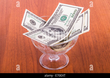 Un centinaio di dollari di banconote in recipiente di vetro su un tavolo di legno.