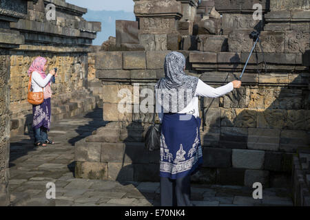 Borobudur, Java, Indonesia. Due giovani donne indonesiane a fotografare il tempio uno usando un palo di estensione. Foto Stock