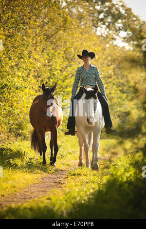 Femmina pilota occidentale su un cavallo di vernice, Nero Tobiano pattern di colori, portando una baia Shagya Arabian horse riding bareback attraverso Foto Stock