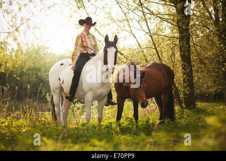 Femmina pilota occidentale su un cavallo di vernice, Nero Tobiano pattern di colori, portando una baia Shagya Arabian horse riding bareback attraverso Foto Stock