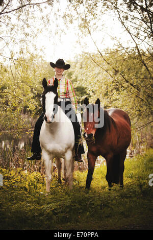 Femmina pilota occidentale su un cavallo di vernice, Nero Tobiano pattern di colori, portando una baia Shagya Arabian horse riding bareback attraverso Foto Stock