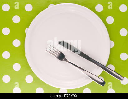 Bianco Vuoto piastra piana con la forchetta e il coltello sul tavolo coperti con panno verde. Foto Stock