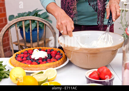 Ritagliato colpo di donna matura preparare frutta flan al party in giardino Foto Stock