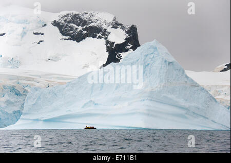 Le persone in piccoli inflatible zodiac barche di nervatura passando iceberg e ice floes in acqua calma Foto Stock
