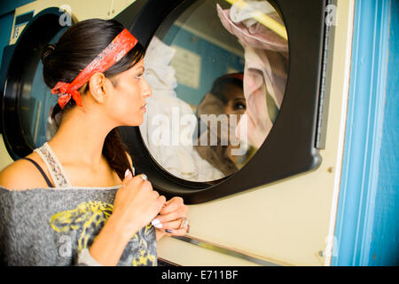 Giovane donna in lavanderia a gettoni, guardando il lavaggio in macchina Foto Stock